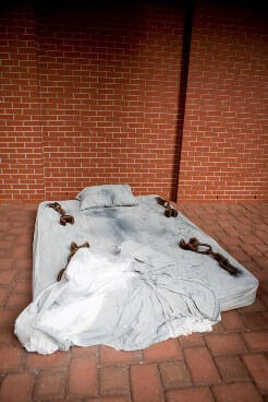 Mattress with sheets, dirty, on a brick floor.